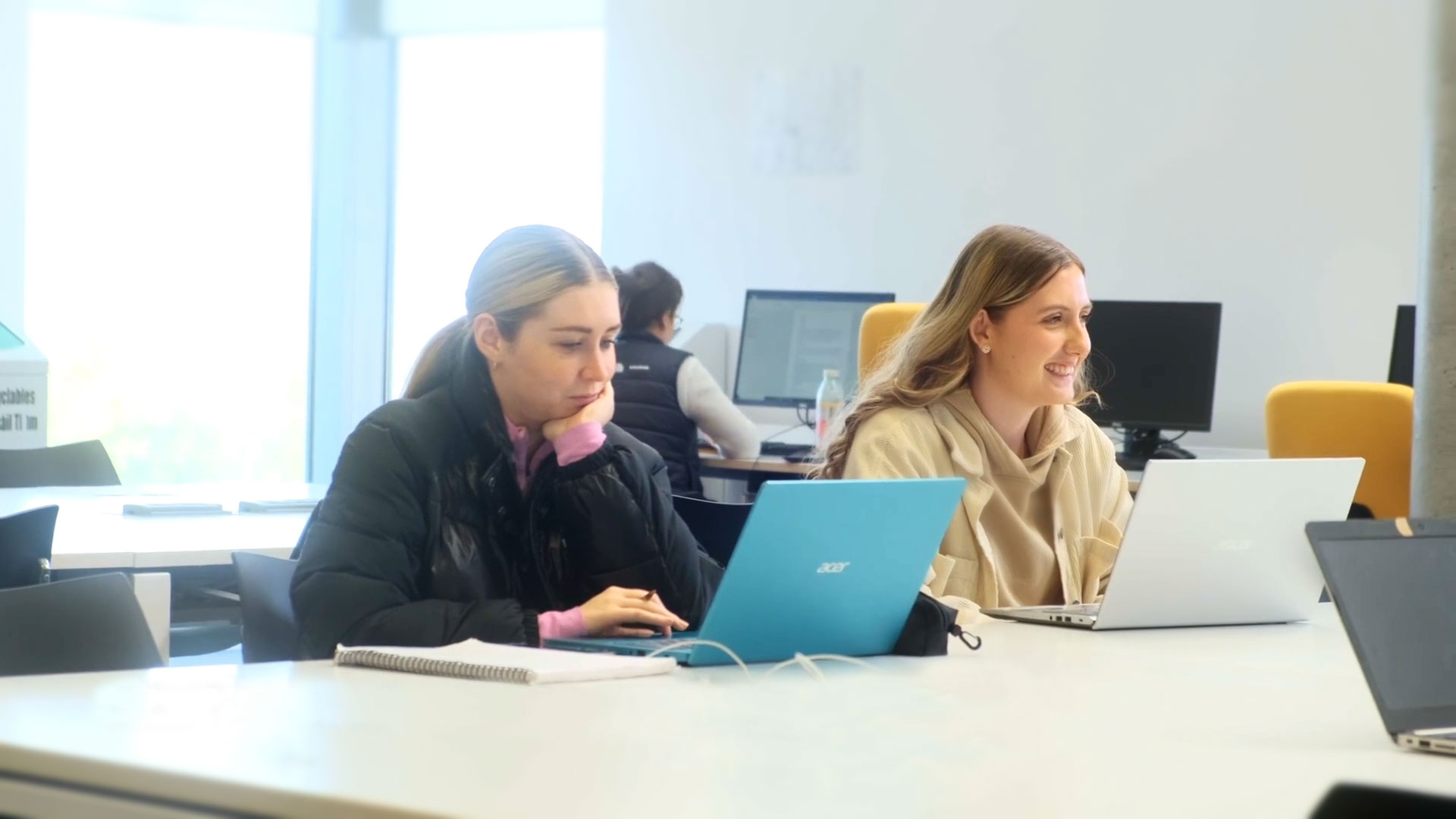 Two female students working together at a desk using laptops.