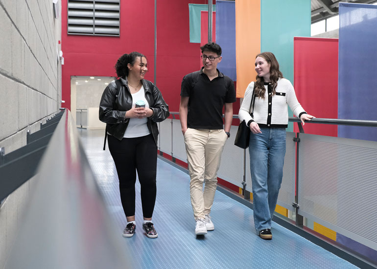 Three students in a campus building walking and chatting