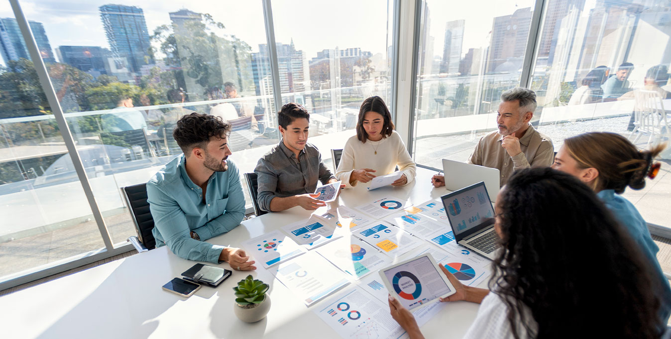 Group of office workers around a meeting room table looking at performance charts